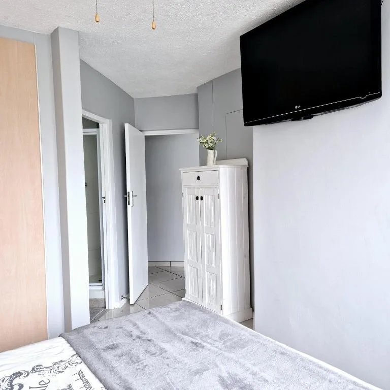 Modern bedroom with wall-mounted TV, white storage cabinet, gray walls