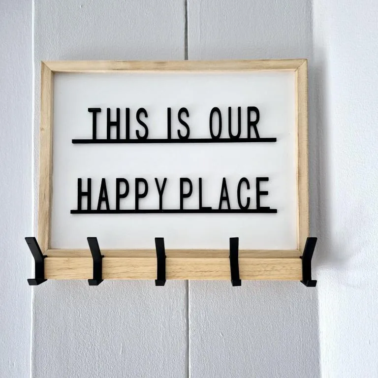 Framed wooden sign reading 'This is our happy place' with hooks