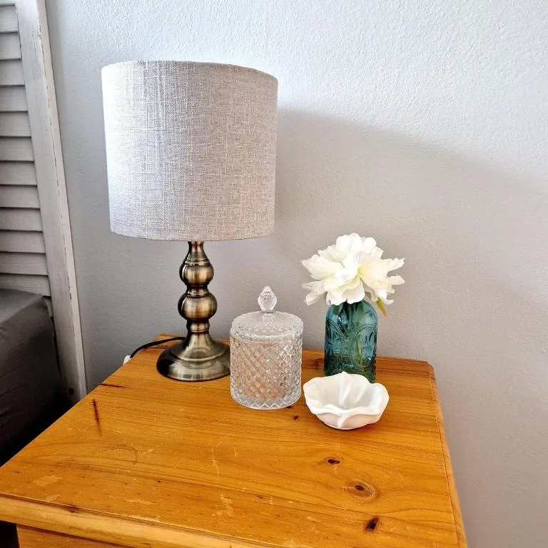 Wooden bedside table styled with brass lamp, crystal jar, and fresh white flowers