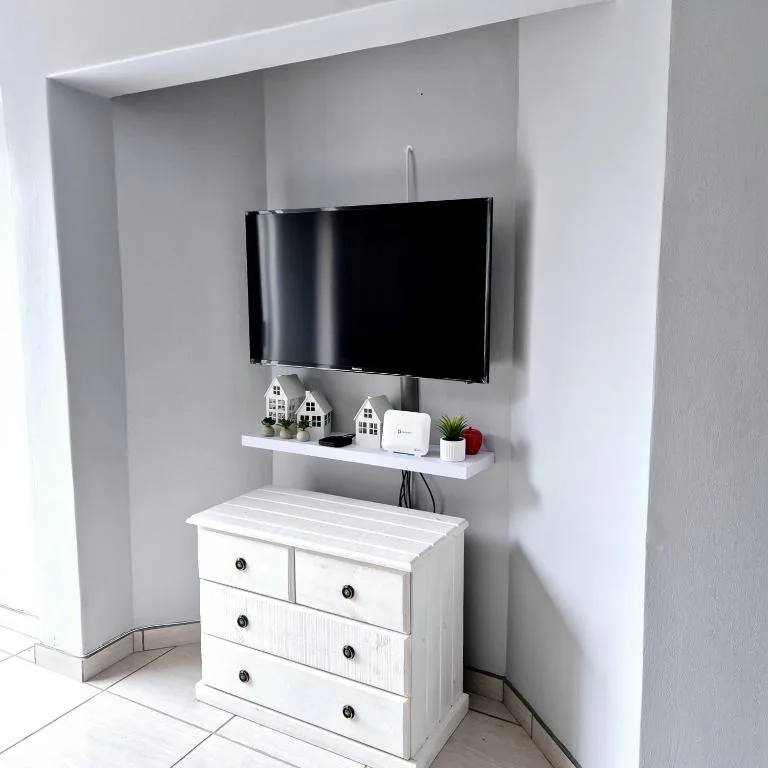 Wall-mounted TV above white dresser with decorative shelf and accessories