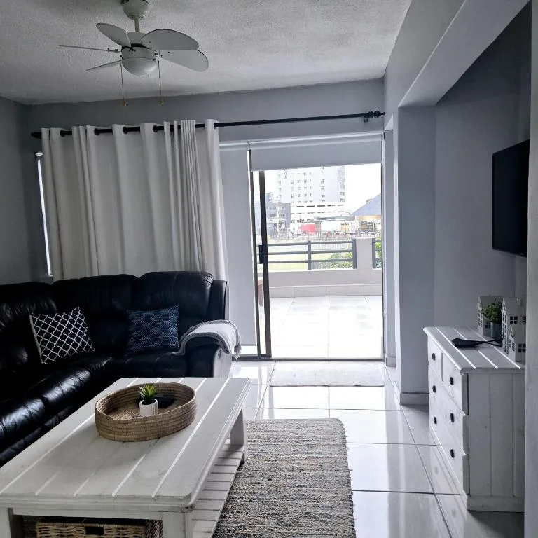Modern lounge with black leather sofa, ceiling fan, and glass door opening to outdoor deck
