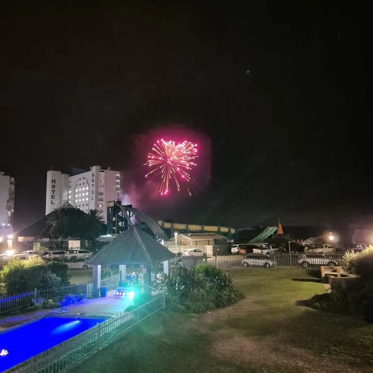 Night view of illuminated pool and deck with fireworks bursting overhead