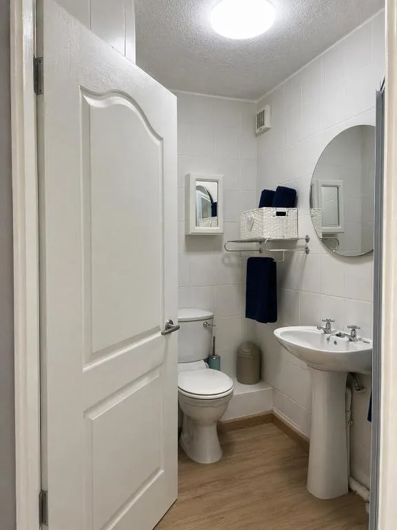 Clean white bathroom with toilet, pedestal sink, and shower enclosure