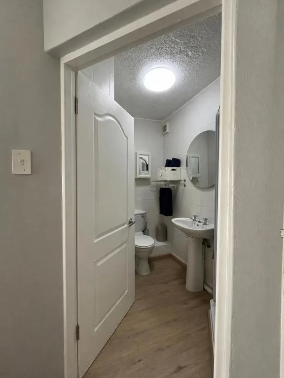 Clean white bathroom with toilet, pedestal sink, and round mirror