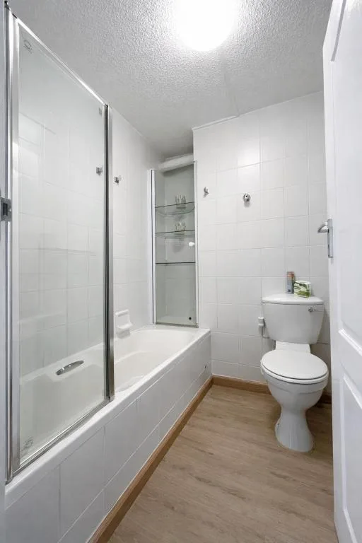 Clean white-tiled bathroom with shower, toilet, and wooden flooring