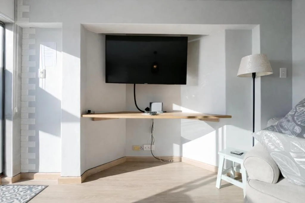 Bright bedroom with mounted TV above wooden desk and natural light