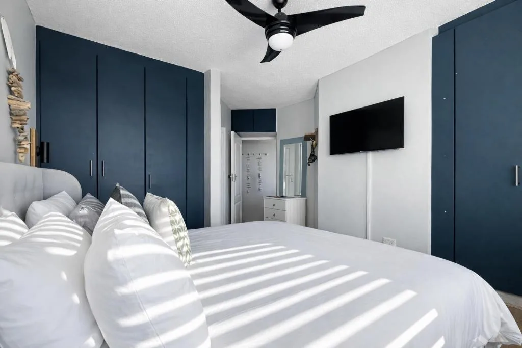 Modern bedroom with king bed, navy built-in wardrobes, wall-mounted TV
