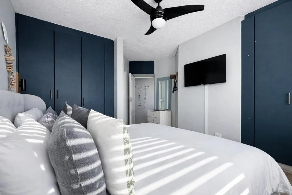 Modern bedroom with white bedding, dark blue built-in wardrobes, ceiling fan