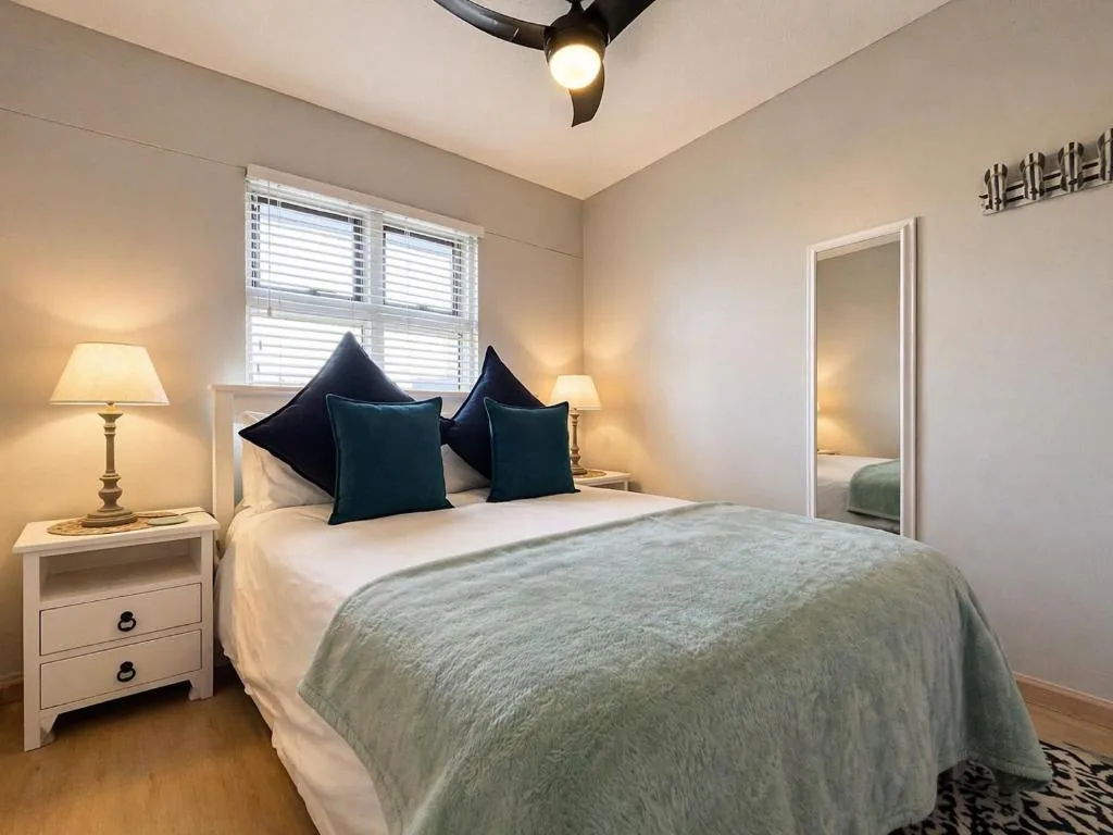 Bright bedroom with queen bed, teal pillows, bedside lamps, wooden floors