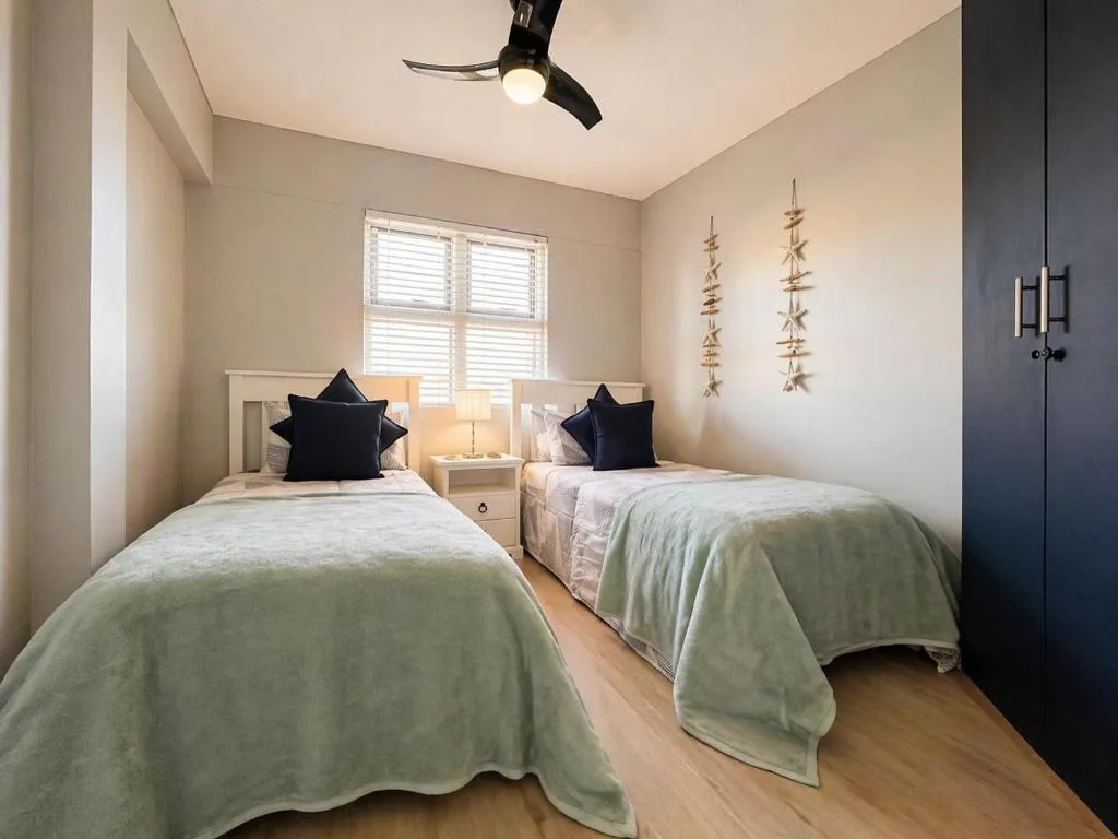Twin bedroom with green bedding, black pillows, coastal decor, and shuttered windows