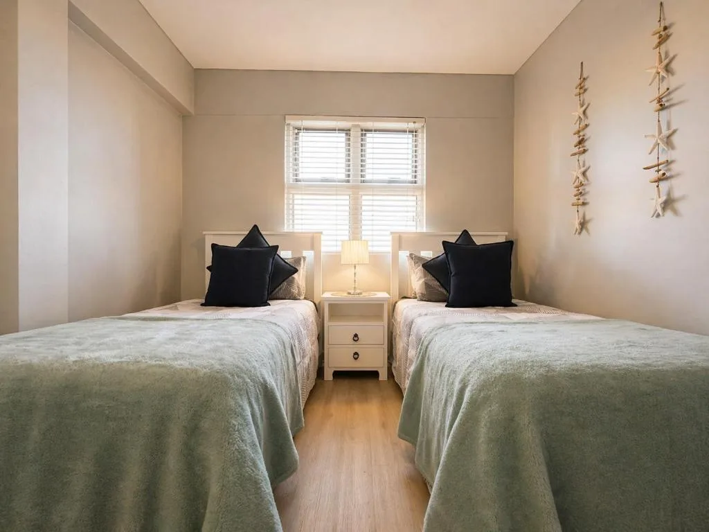 Twin bedroom with two single beds, black pillows, and shared bedside table lamp