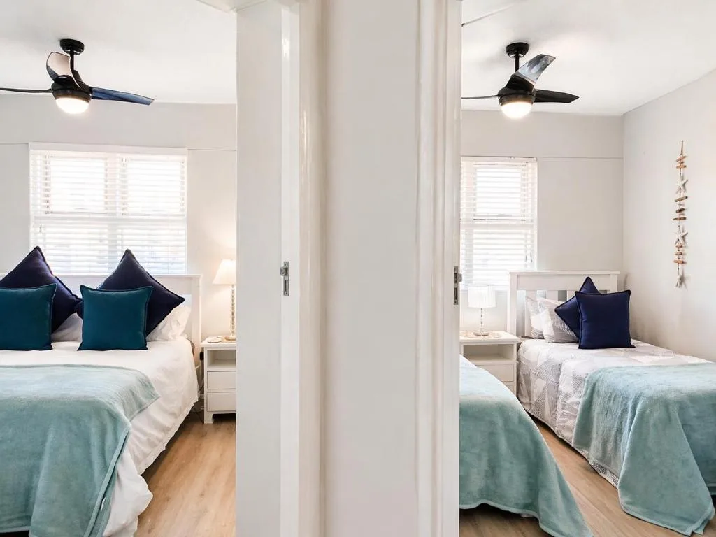 Twin bedroom with teal bedding, dark pillows, and ceiling fans