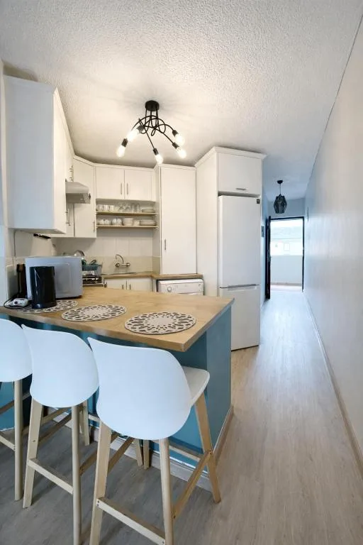 Modern kitchen with white cabinetry, wooden counter, and bar seating