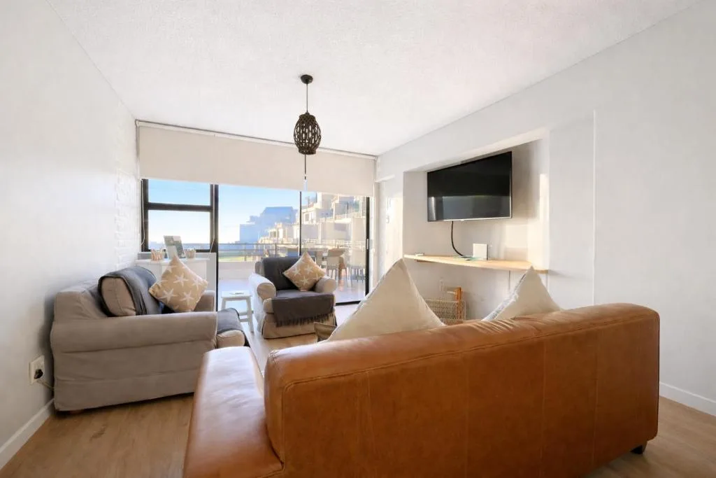 Modern lounge with leather sofas, mounted TV, and panoramic ocean views