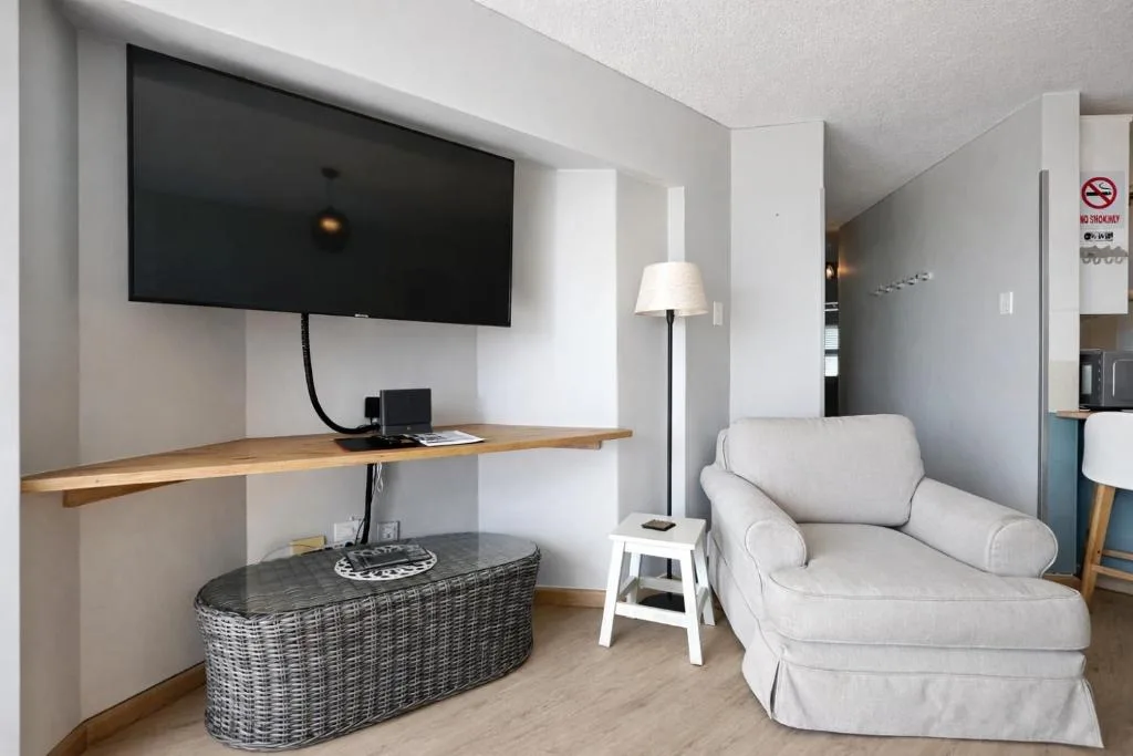 Modern lounge with wall-mounted TV, cream armchair, and wooden desk workspace