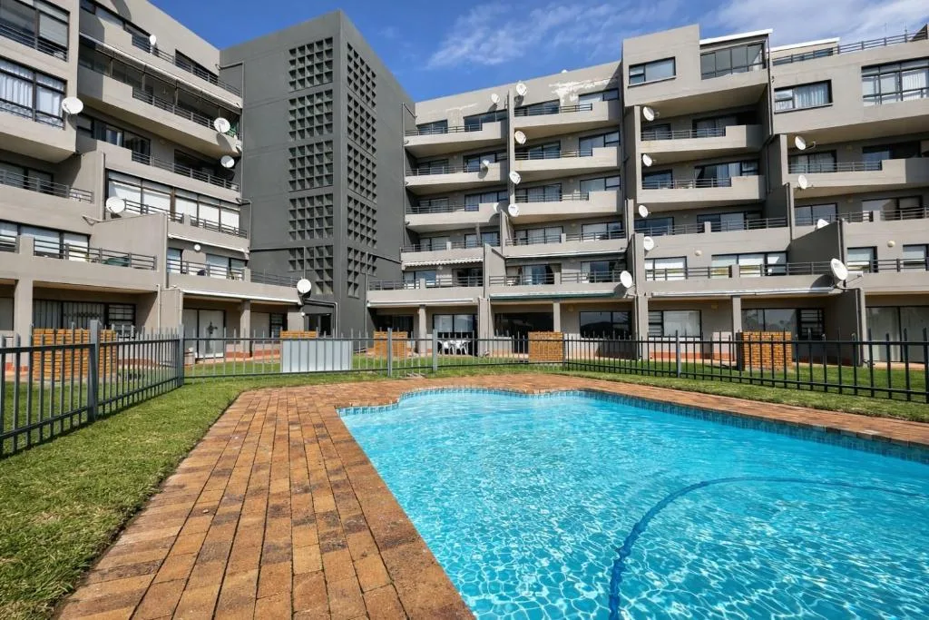 Sparkling blue swimming pool with brick deck and apartment building beyond