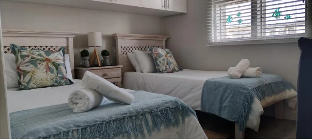 Twin bedroom with white headboards, floral pillows, and rolled towels on beds