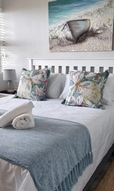 Bright bedroom with white bed frame, floral pillows, and coastal artwork above headboard