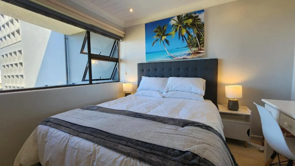 Bright bedroom with queen bed, dark headboard, and tropical wall art