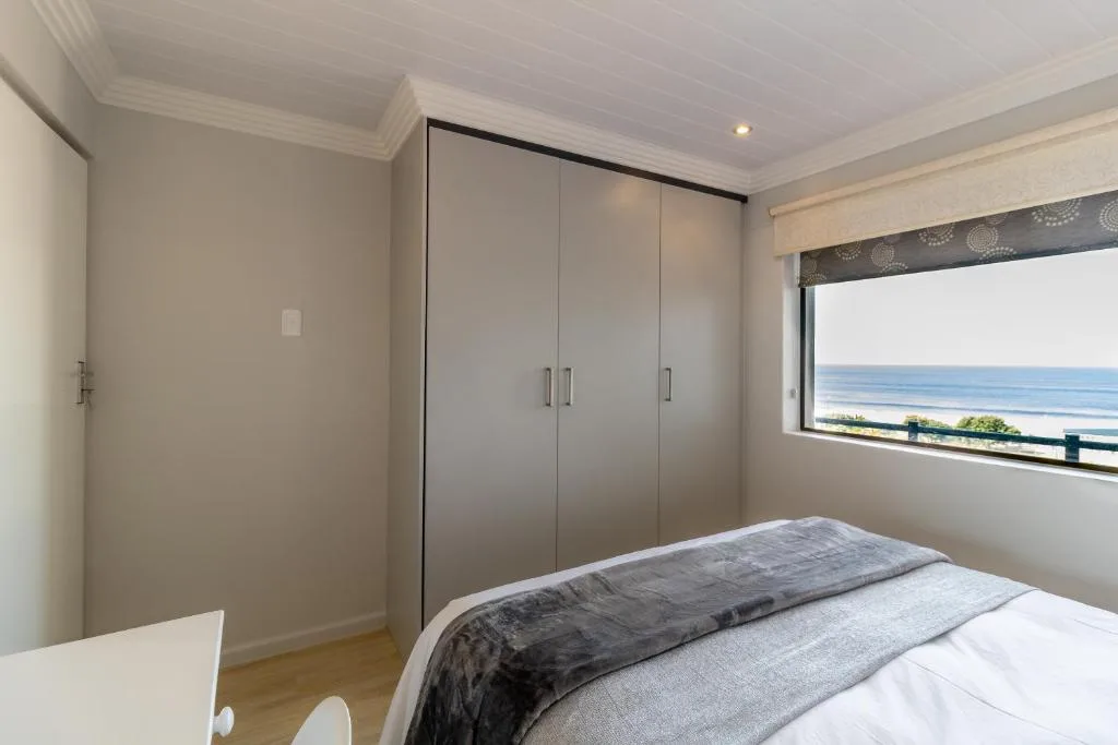 Bright bedroom with ocean view, built-in wardrobe, and coastal landscape visible through window