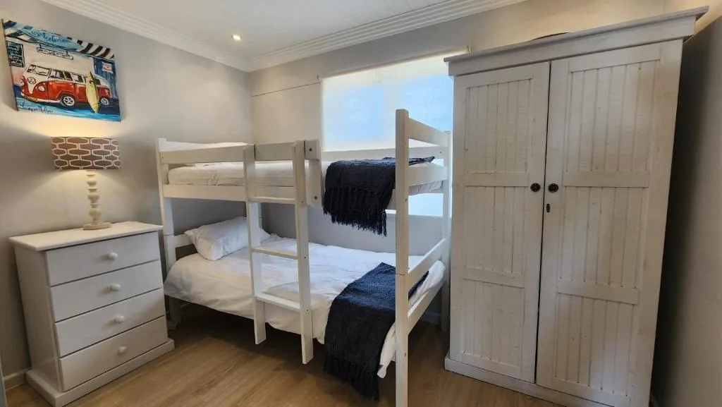 Bright bedroom with white bunk beds, dresser, and wardrobe closet
