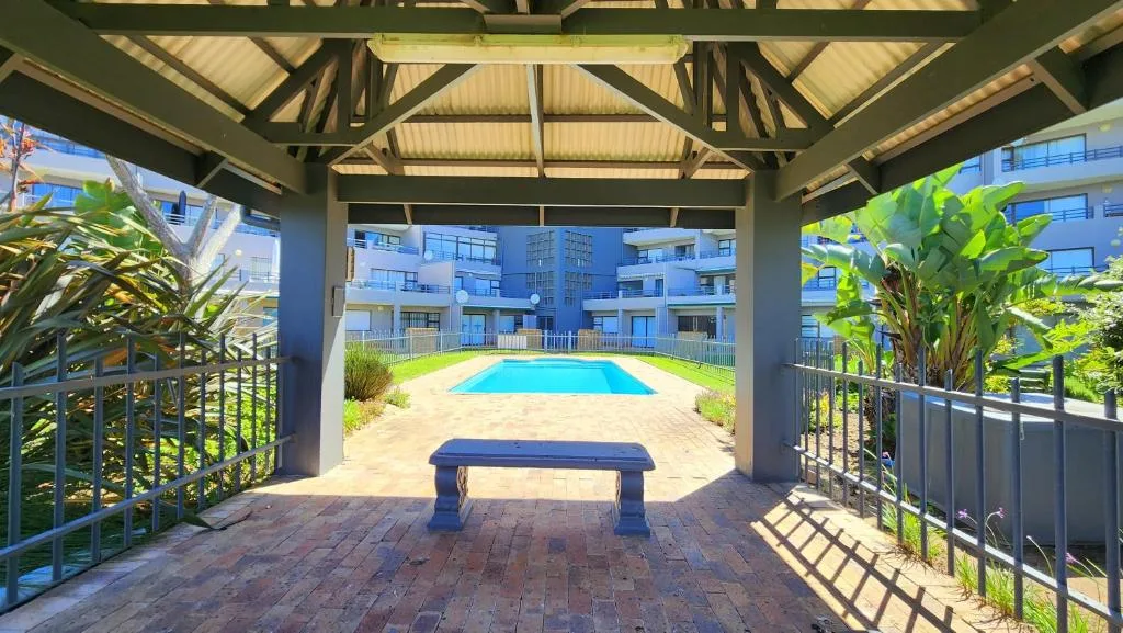Covered braai area with blue bench overlooking communal pool and gardens