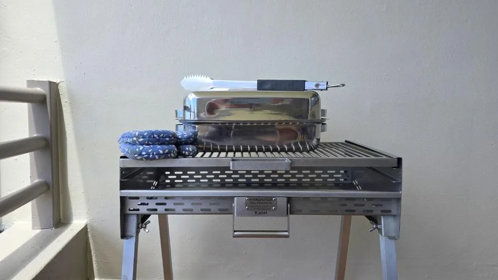 Braai grill with cooking utensils and blue cloth nearby