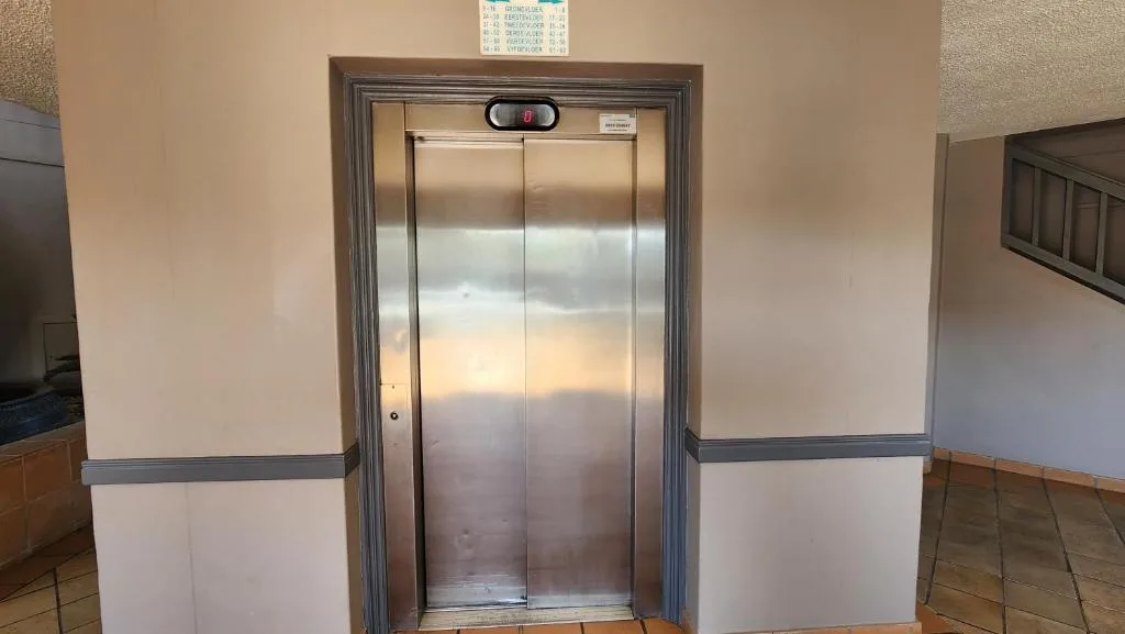 Stainless steel elevator doors in neutral-toned hallway with wooden flooring