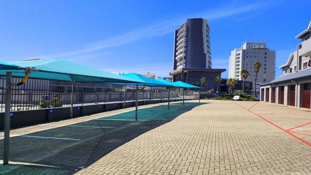 Paved courtyard with turquoise shade structure and apartment buildings beyond