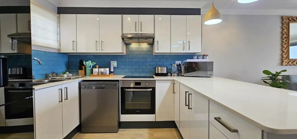 Modern kitchen with white cabinetry, blue tile backsplash, stainless steel appliances