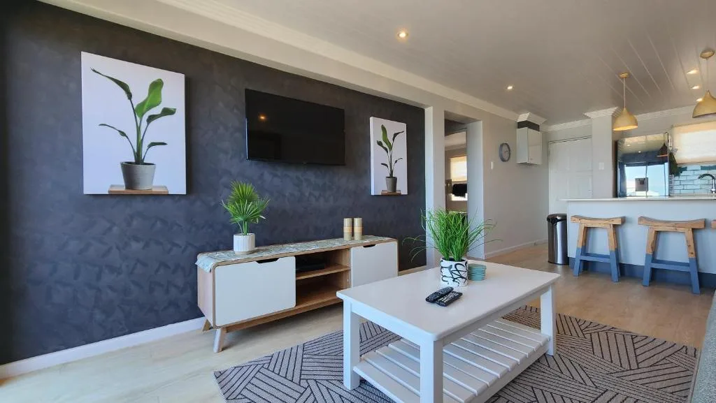 Modern living room with dark blue accent wall, TV, white furniture, and plants