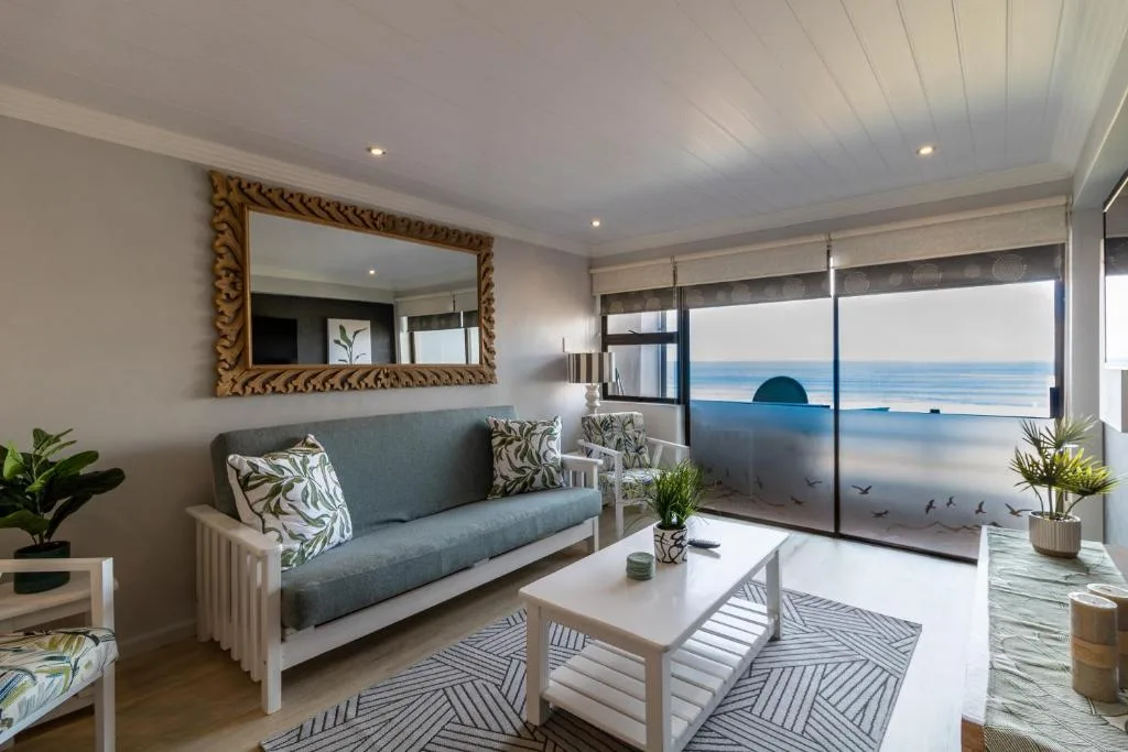 Modern lounge with grey sofa, ocean view through glass doors, decorative mirror