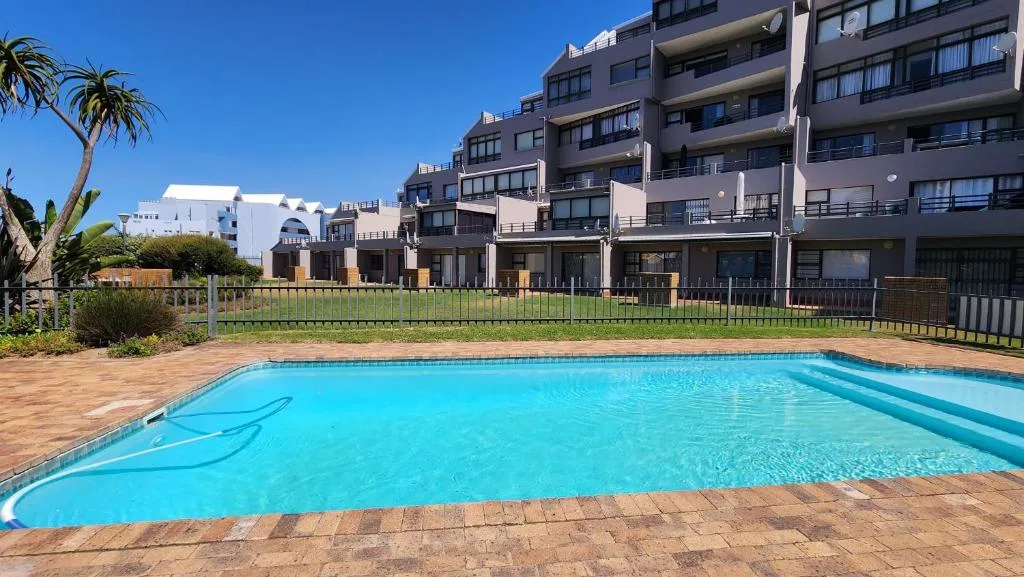 Bright blue swimming pool with brick surround and residential buildings beyond