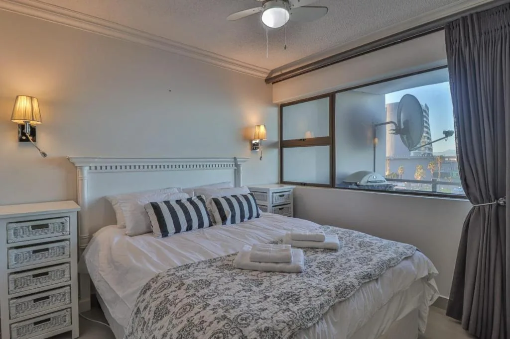 Modern bedroom with queen bed, striped pillows, and large windows overlooking town