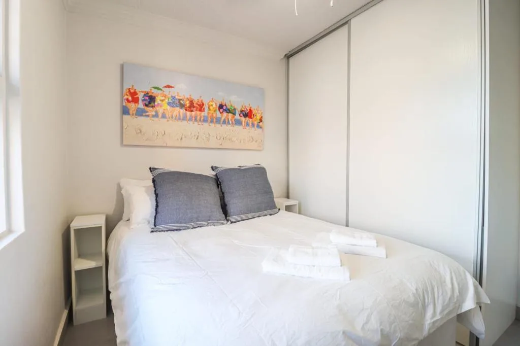 Bright bedroom with white bed, blue pillows, beach artwork, and sliding wardrobe