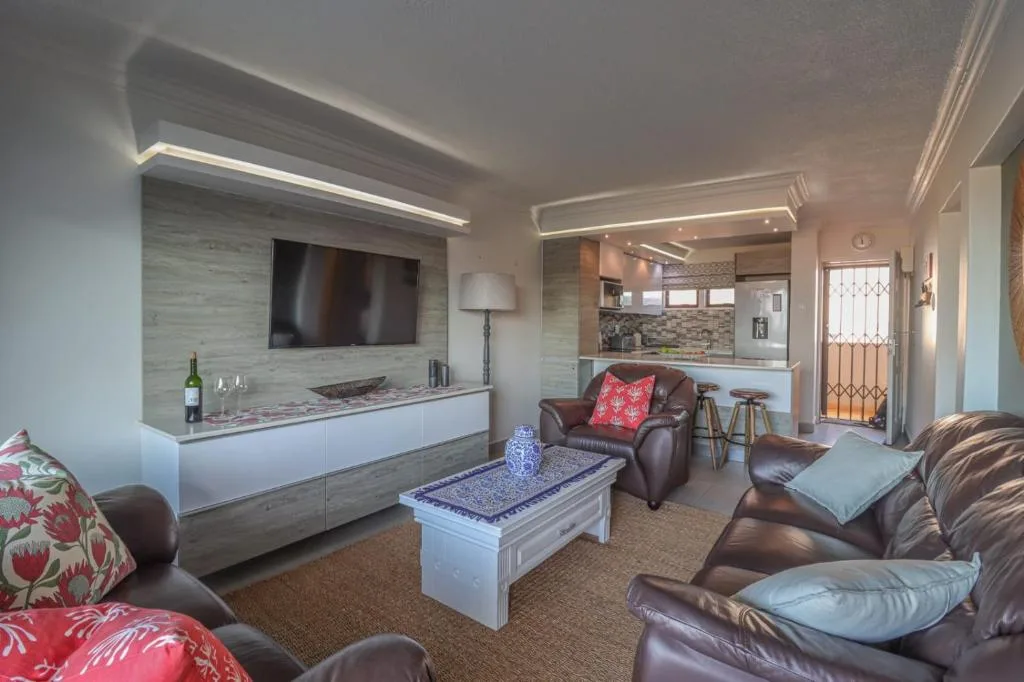 Open-plan lounge with leather sofas, wall-mounted TV, and kitchen view