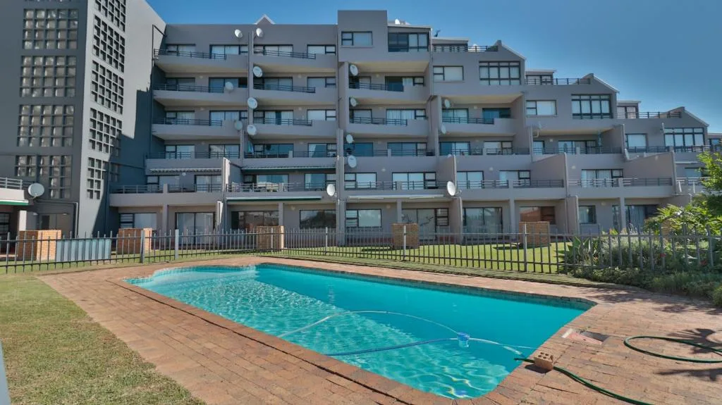 Bright turquoise swimming pool with apartment building and manicured lawn behind