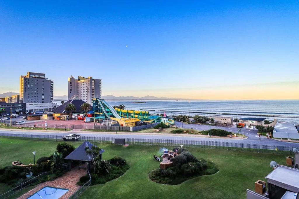 Scenic coastal view of Mossel Bay beach with ocean, mountains, and waterpark