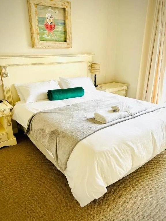 Bright bedroom with white bedding, green accent pillow, and framed artwork