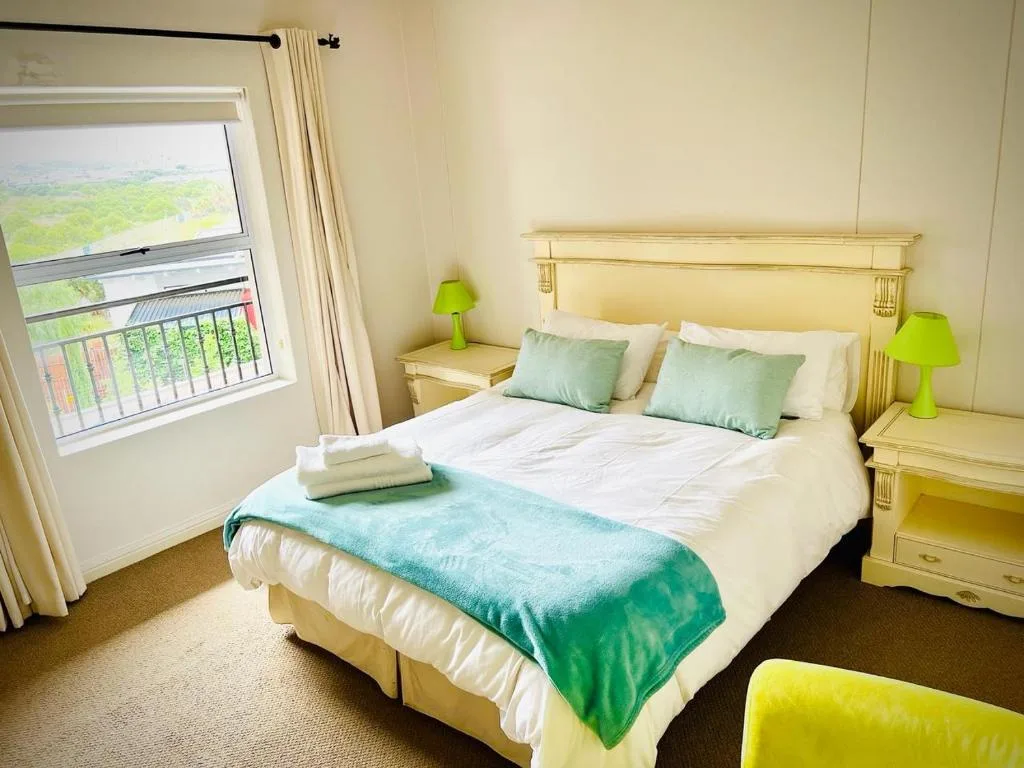 Bright bedroom with queen bed, green accents, and garden view window