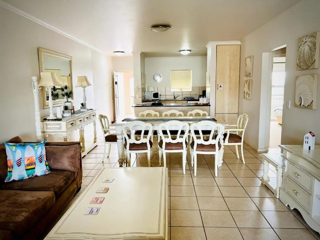 Open-plan dining area with white chairs and kitchen visible beyond