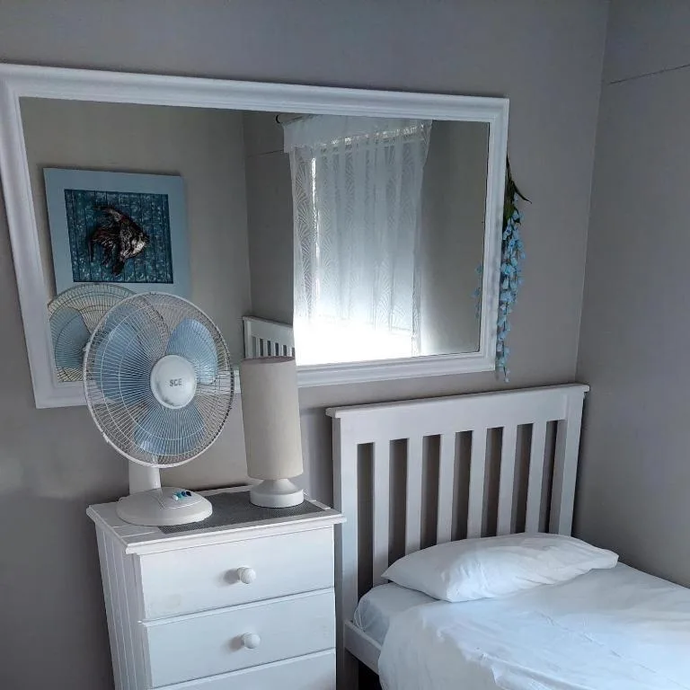 Bright bedroom with single bed, white nightstand, and portable fan