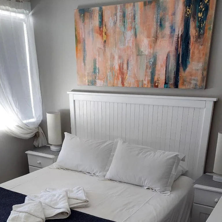 Bright bedroom with white headboard, pillows, and modern abstract artwork above bed