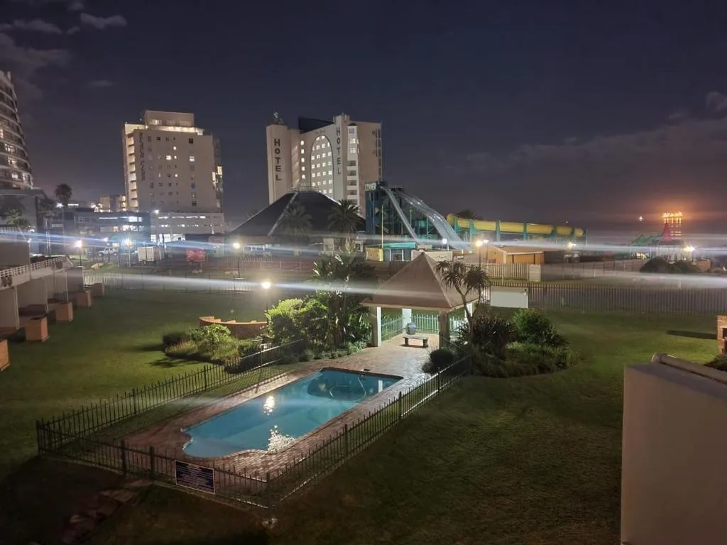 Illuminated swimming pool at night with manicured lawn and beach promenade