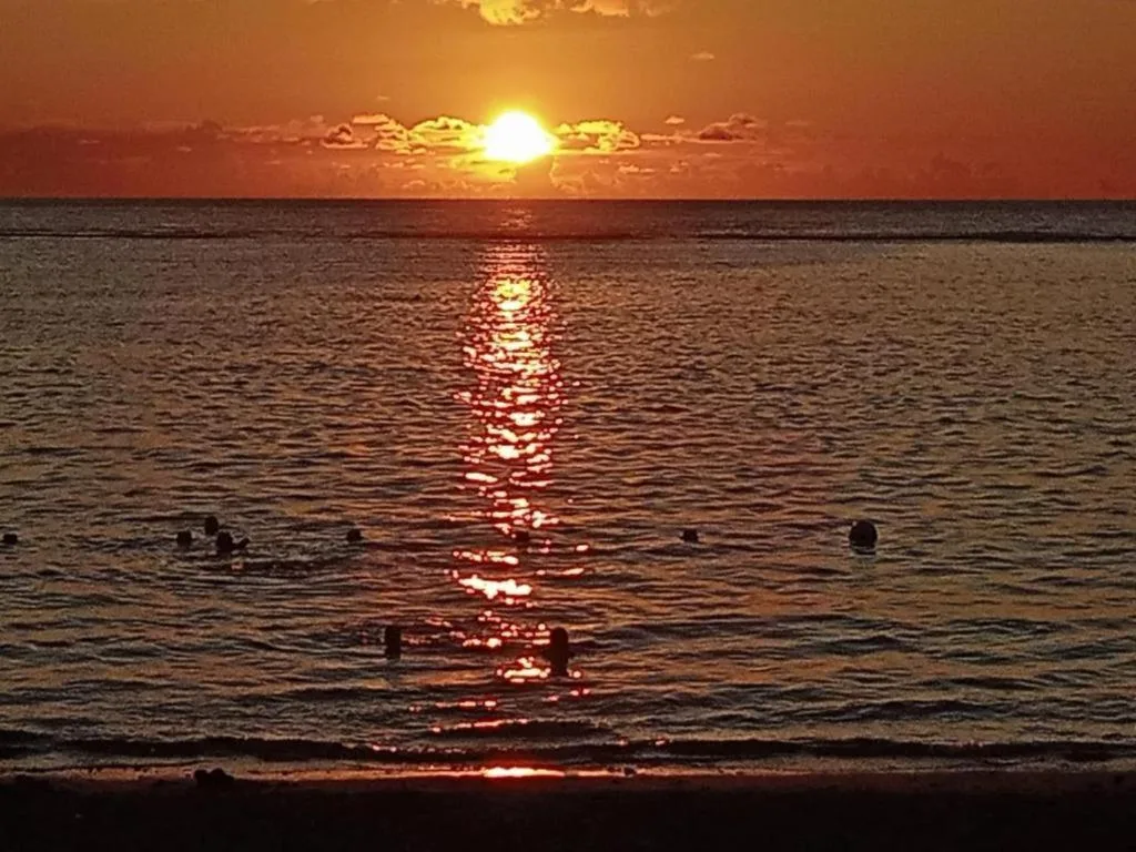 Golden sunset over calm ocean with swimmers enjoying the beach