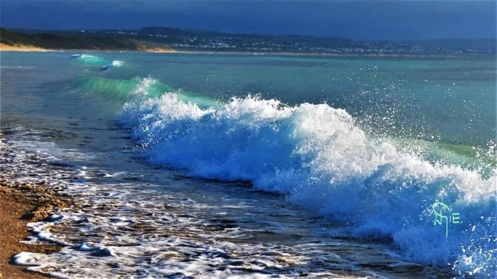 Turquoise ocean waves crashing on sandy beach with coastal hills