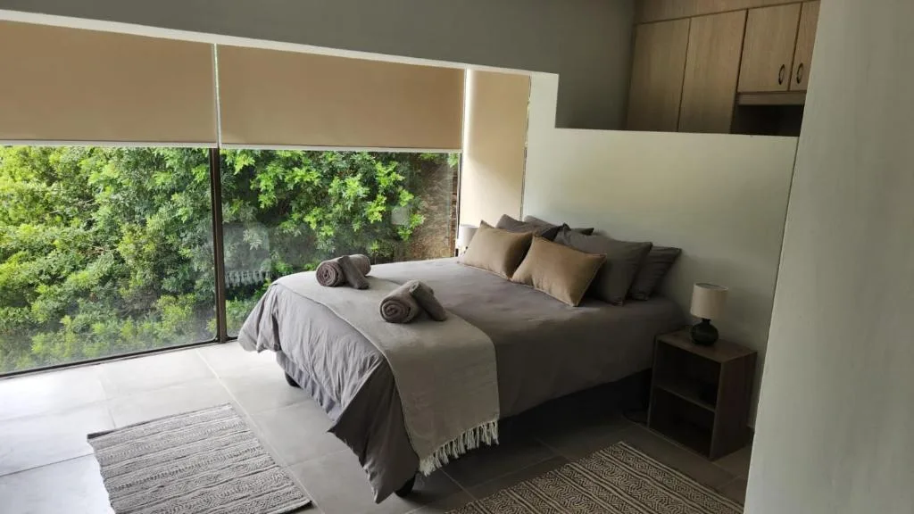Modern bedroom with queen bed, rolled towels, and forest views through large windows