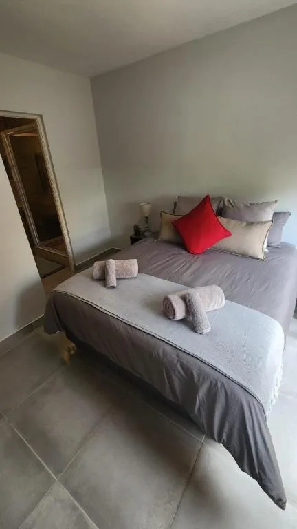 Neat bedroom with gray bedding, red accent pillow, and fresh towels