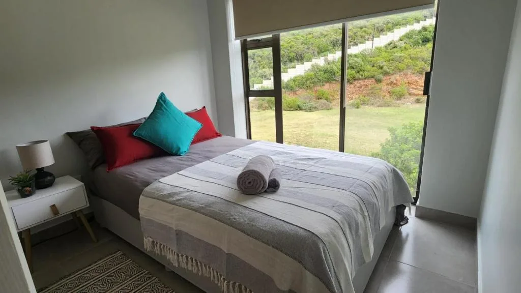 Bright bedroom with queen bed, colorful cushions, and vineyard views through glass doors
