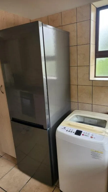 Modern stainless steel refrigerator and washing machine in tiled kitchen area